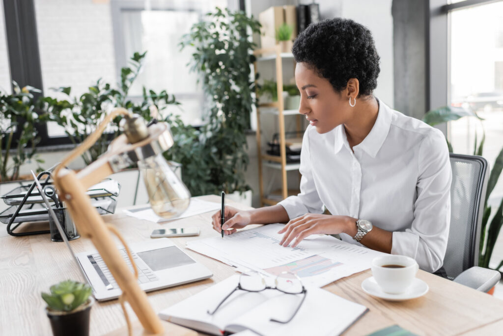 A professional woman working on a sales plan while reviewing notes at her desk.